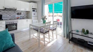 A modern kitchen with white cabinets, a built-in oven, and a microwave. There is a dining area with a white table and chairs, and a TV mounted on the wall. - 523 center Playa las Americas, pool and wifi (Playa de las Américas)