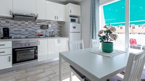 A modern kitchen with white cabinets, a built-in oven, and a dining area with a white table and chairs. - 523 center Playa las Americas, pool and wifi (Playa de las Américas)