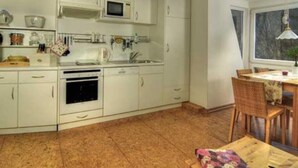 A kitchen with white cabinets, a microwave, and a dining area with a table and chairs. - Cosy Apartment in Harz (Kassel)