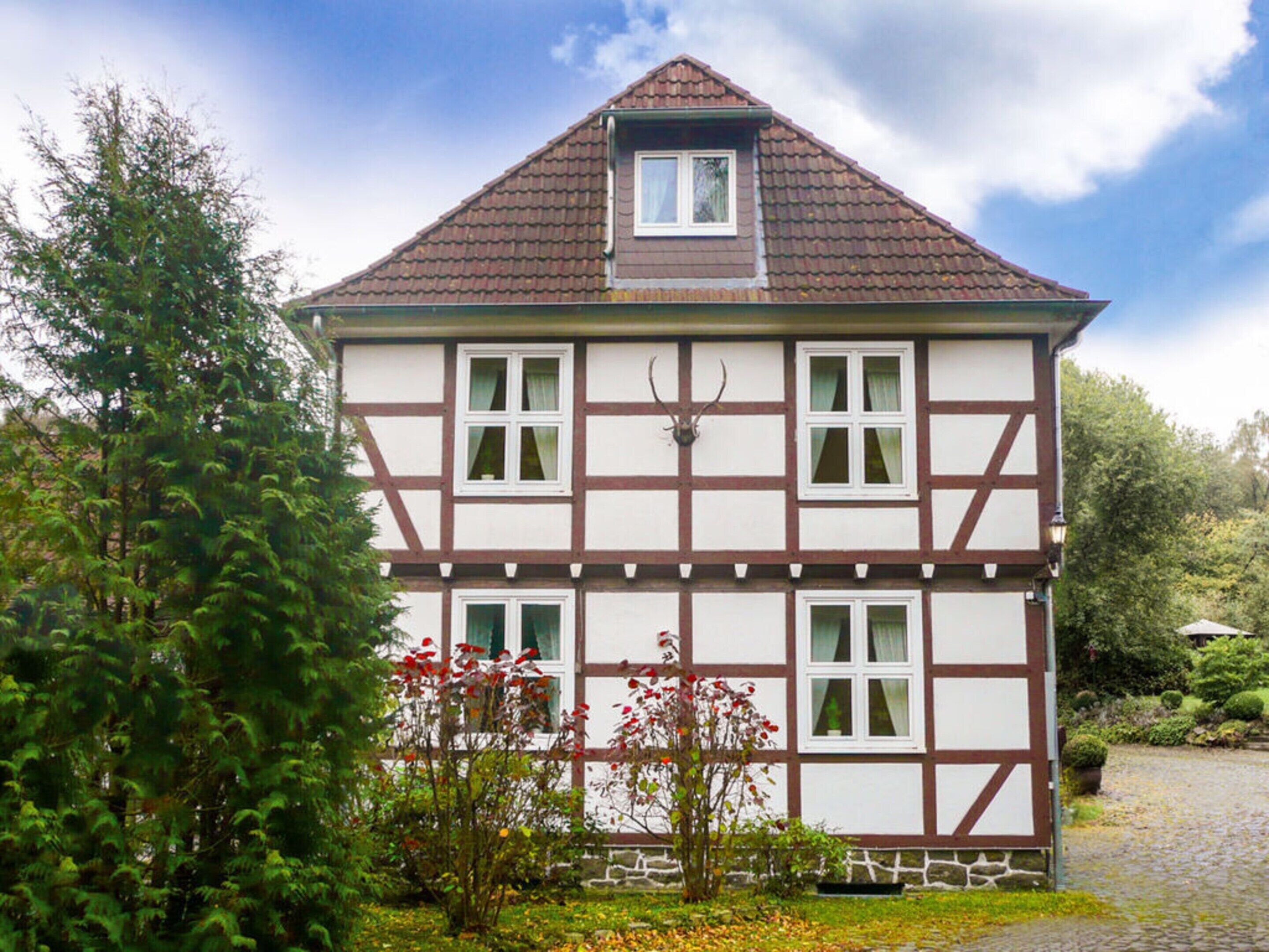 A traditional half-timbered house with a steeply pitched roof, multiple windows, and a small balcony.