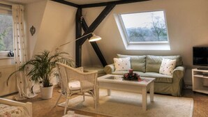 A cozy living room with a sofa, a coffee table, a chair, a potted plant, and a TV. - Cosy Apartment in Harz (Kassel)
