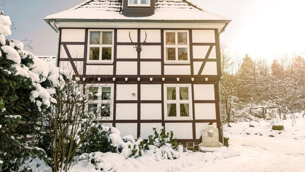 A two-story Tudor-style house with a steeply pitched roof, dormer windows, and a stone foundation. - Cosy Apartment in Harz (Kassel)