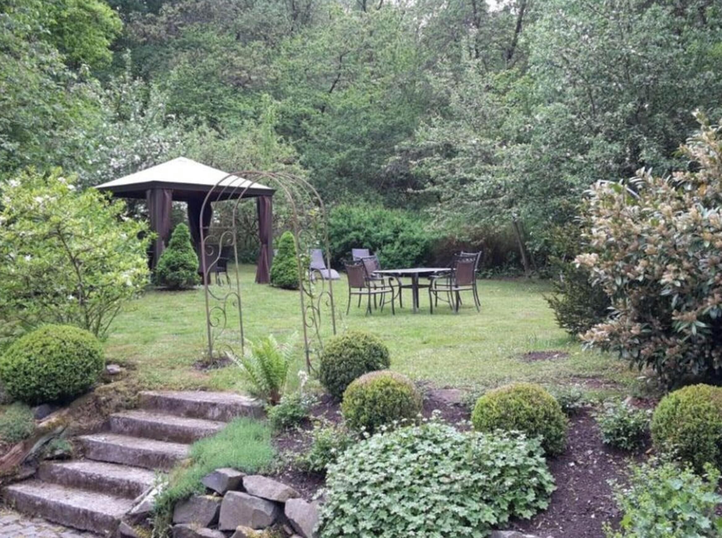 Un jardín con un pabellón, una mesa con sillas y una escalera de piedra.
