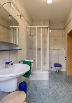 Et badeværelse med brusebad, vask, toilet og et spejl.