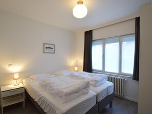 Habitación de hotel con dos camas, una mesita de noche, una lámpara, un cuadro en la pared y una ventana con cortinas.