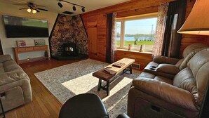 Una sala de estar acogedora con chimenea de piedra, muebles de cuero, televisor de pantalla plana y vistas al exterior.