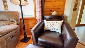 Una habitación acogedora con un sillón de cuero, una lámpara de pie y un cojín decorativo con un mensaje.