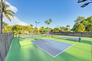 Ein Tennisplatz mit grüner Belag, umgeben von Palmen und blauem Himmel.