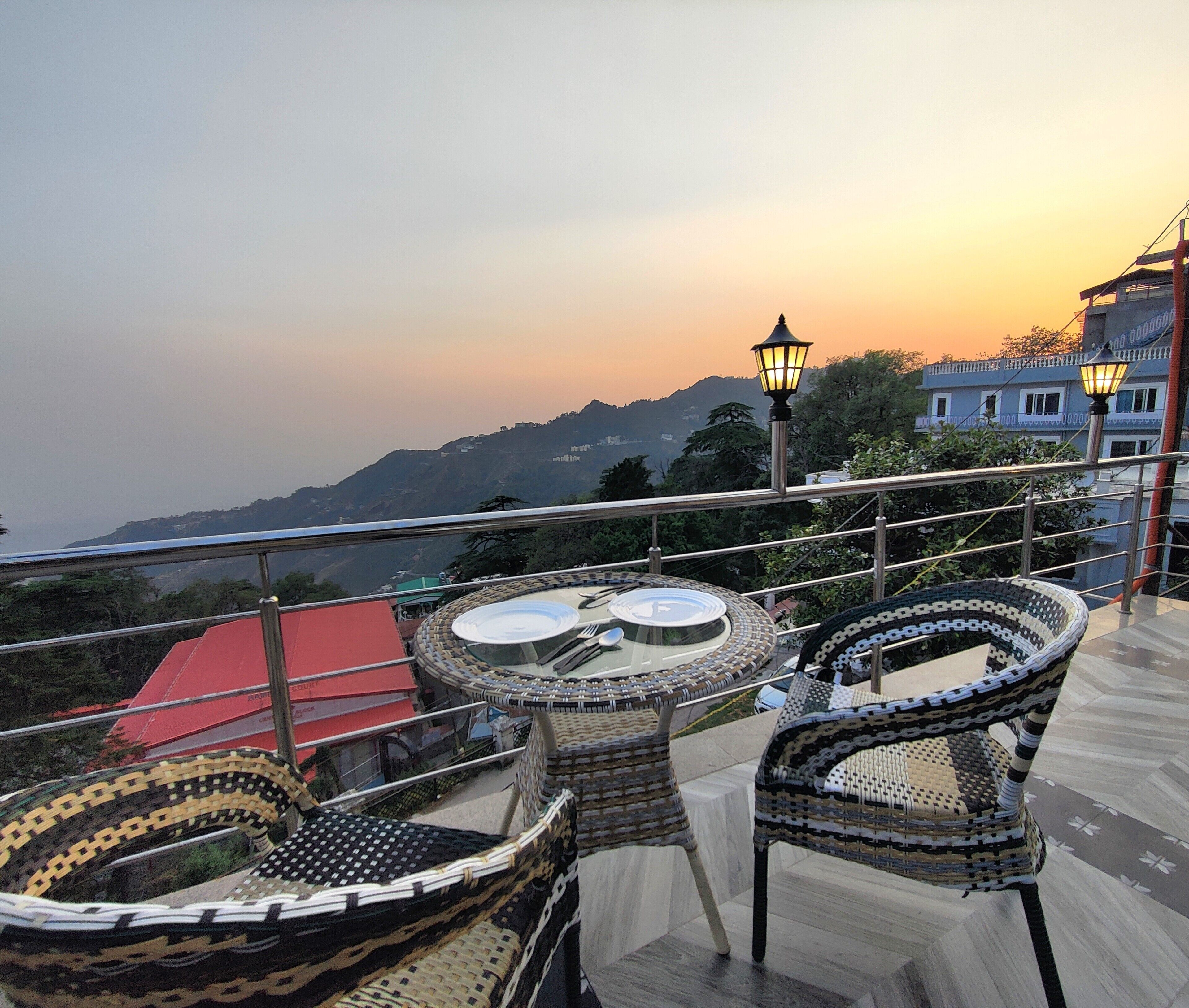 A terrace with wicker furniture and a view of a mountainous landscape during sunset.