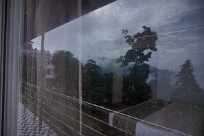 A view through a window with a metal railing, a tiled floor, and a reflection of trees and buildings. - Sangam by Stotrak (Dehradun)