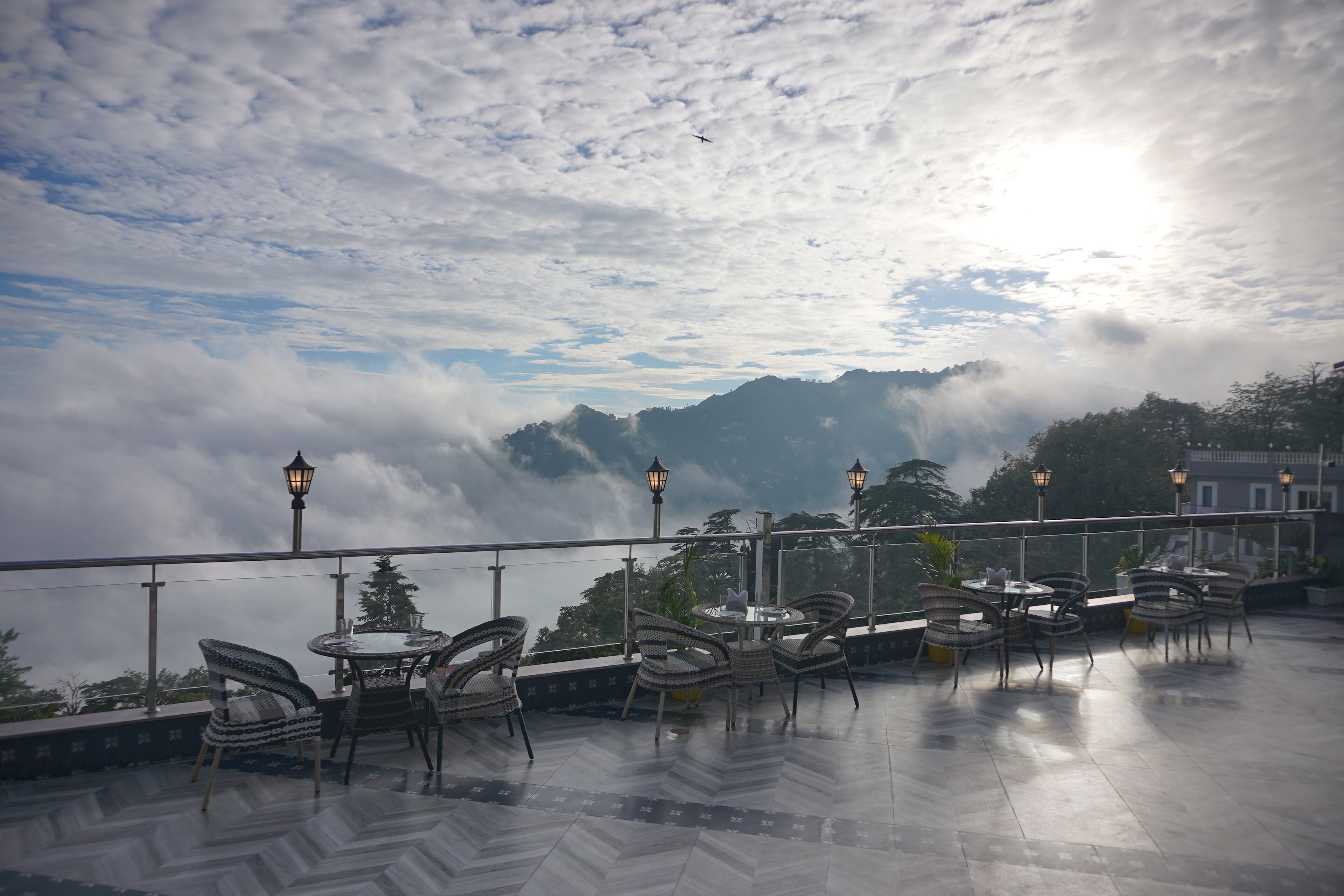 Una terrazza con sedie e tavoli in vimini, affacciata su un paesaggio montuoso con nuvole e vista sul mare.