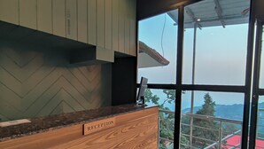 Un comptoir d’accueil avec un sol à motifs en chevrons, un comptoir en bois et une vue sur un bâtiment à toit rouge, visible à travers une porte vitrée.