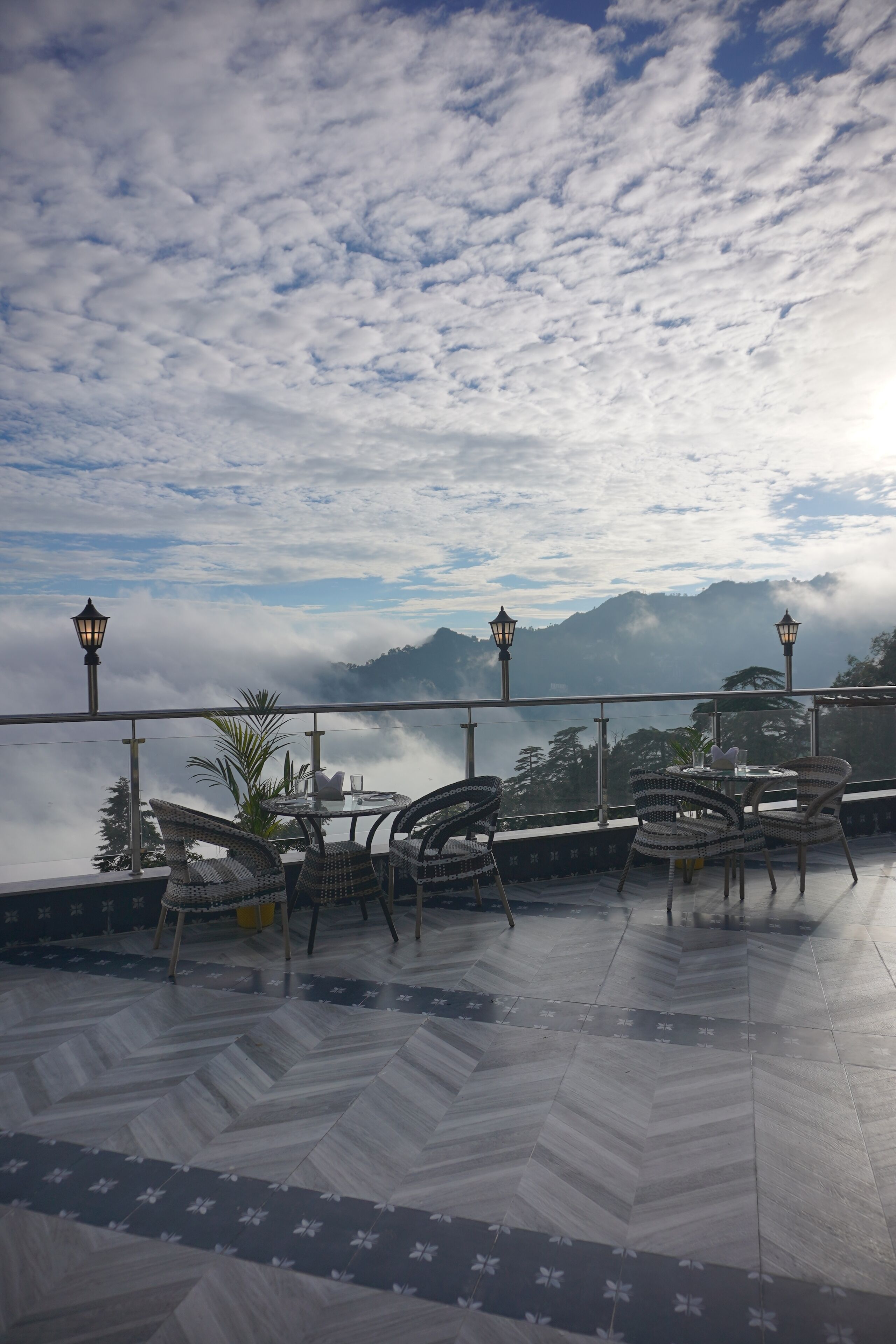 Une terrasse avec des chaises et une table en osier, d’où l’on peut admirer un paysage montagneux et les nuages.