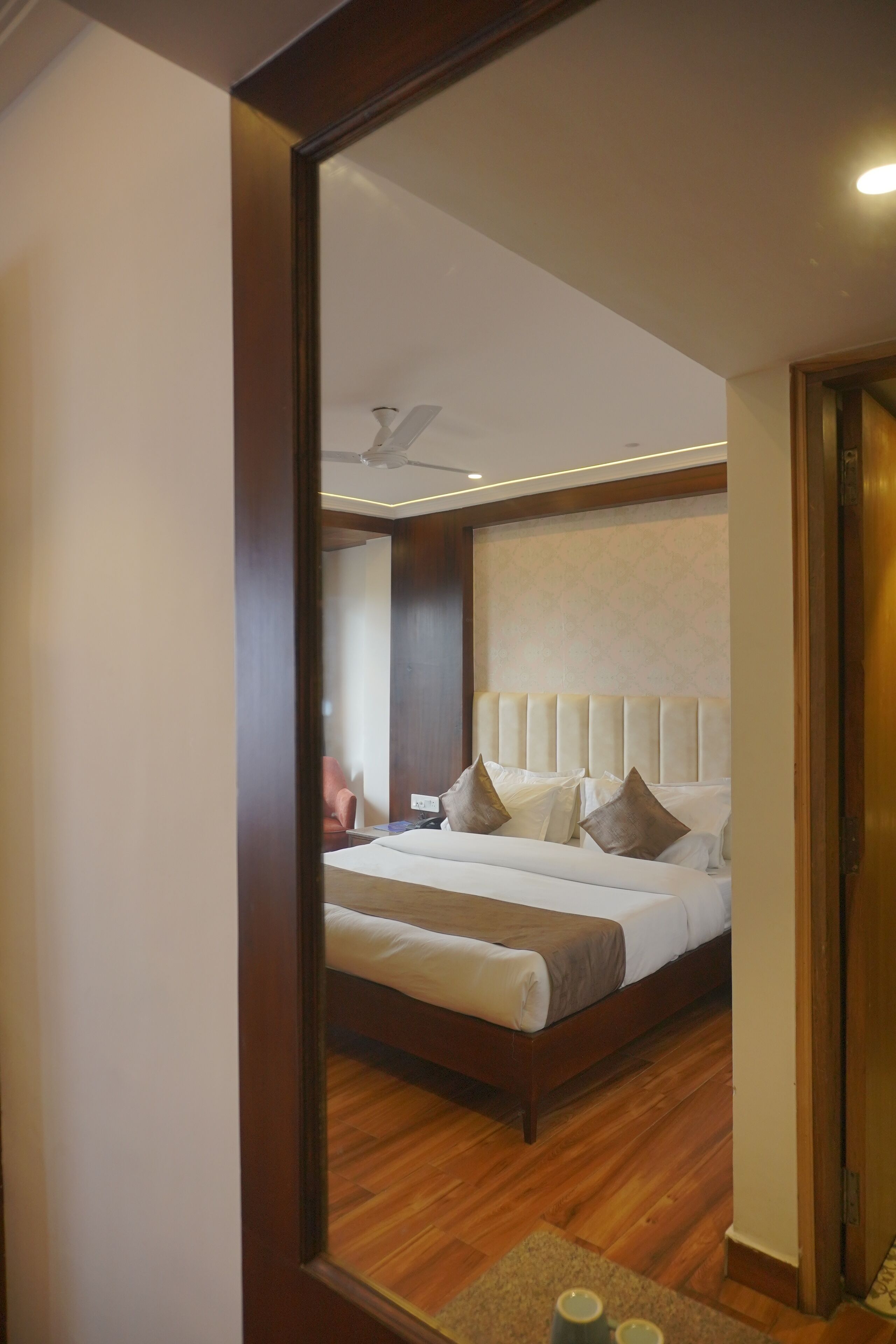 A hotel room with a large bed, a wooden floor, a headboard, and a bedside table with a lamp.