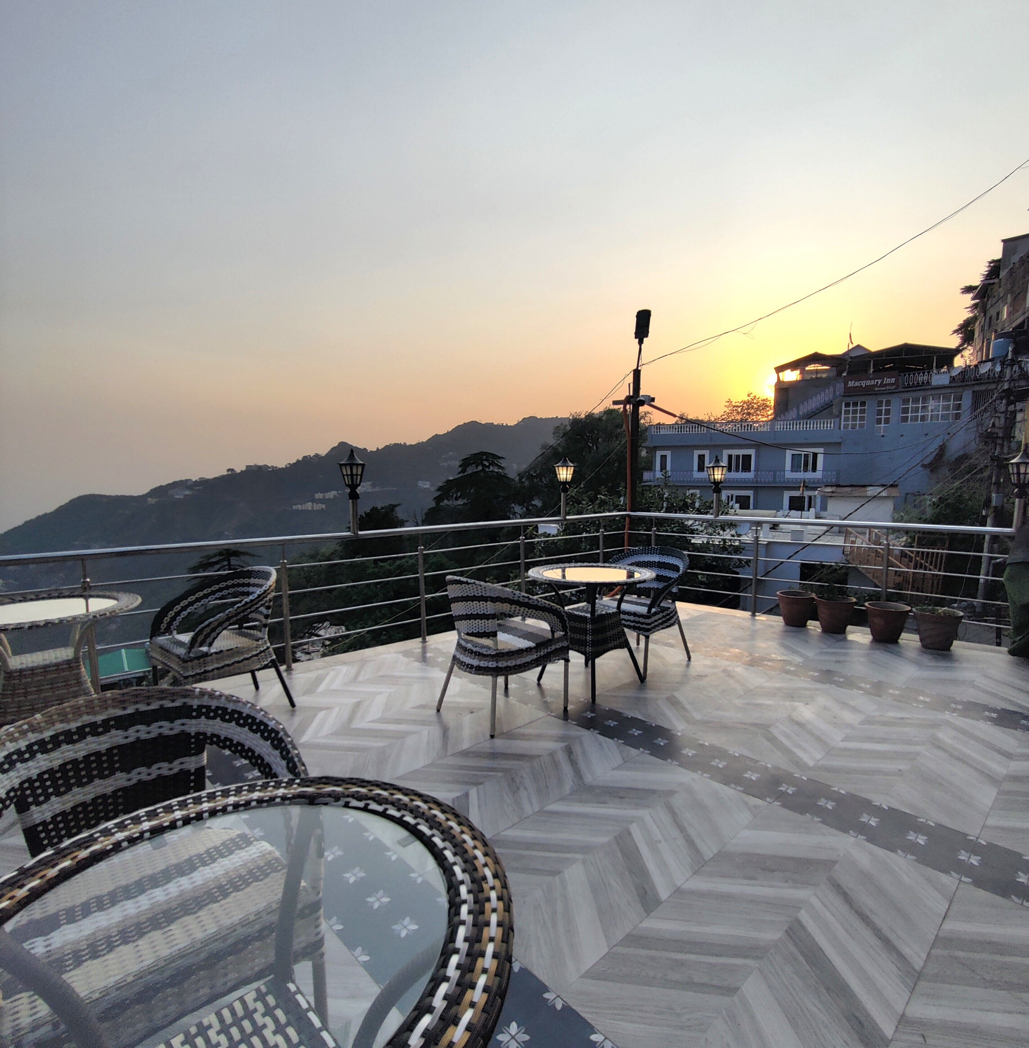 A terrace with outdoor seating and a view of the sunset over a hilly landscape.