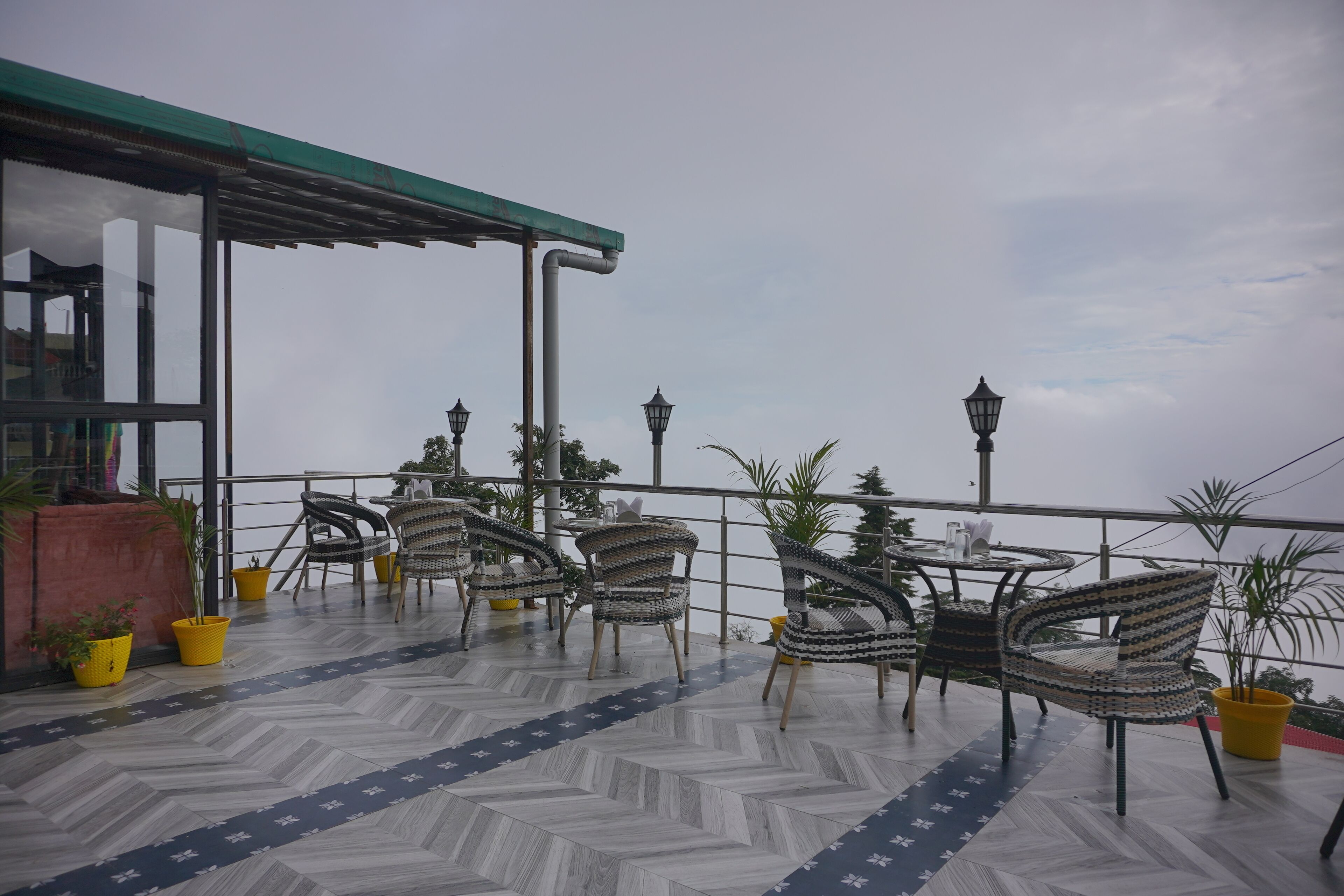 Una terraza al aire libre con suelo estampado, sillas de mimbre, macetas amarillas con plantas y un toldo verde.