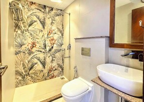 A bathroom with a shower curtain featuring a tropical leaf pattern, a white toilet, a sink with a granite countertop, and a mirror above the sink. - Sangam by Stotrak (Dehradun)