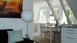A cozy living room with a painting of a deer, a white lamp, and a dining area with a table and chairs. - Apartment at the Eichenpark (Egestorf)