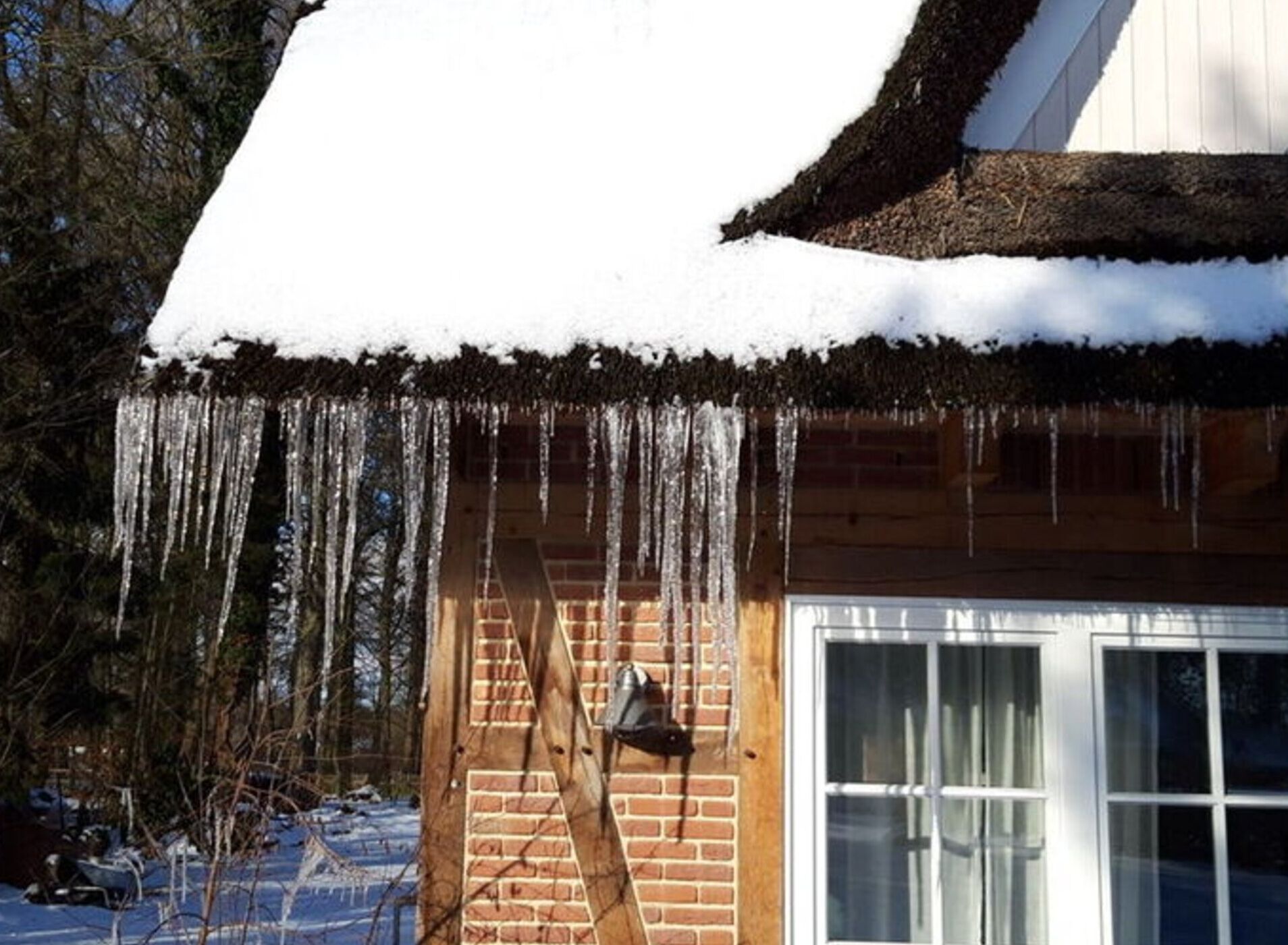 Una casa de madera con techo cubierto de nieve y cascabeles de hielo colgando de los aleros.
