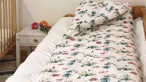 A bed with a floral-patterned bedspread and matching pillow, a wooden headboard, and a nightstand with a vase of flowers. - 8 Person Holiday Home in Nordfold-by Traum (Steigen)