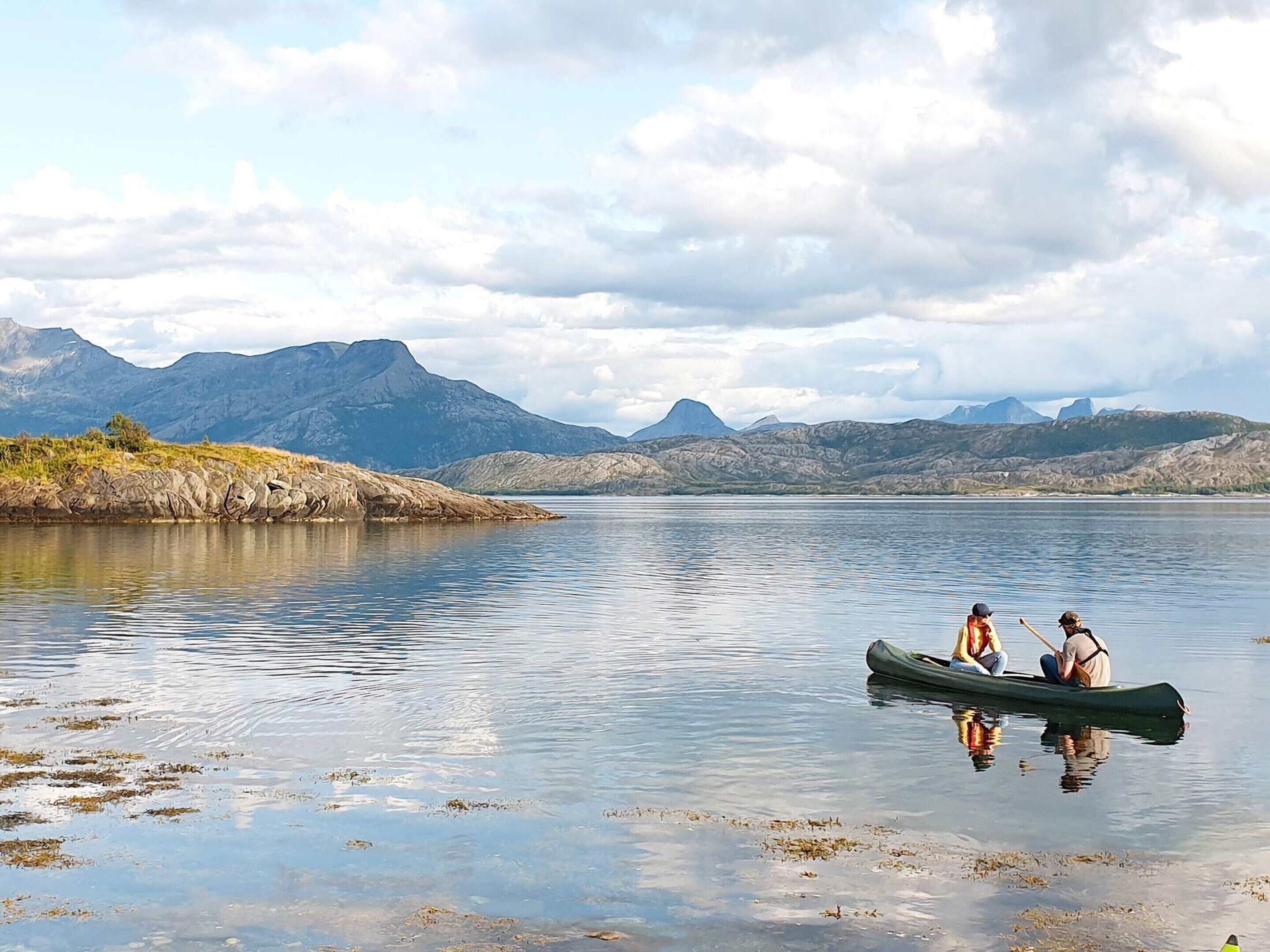 A calm lake with a canoe and two people paddling, surrounded by mountains and clear skies.