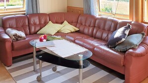 A spacious living room with a large leather sofa, a glass coffee table, and a view of a green landscape through the windows. - 8 Person Holiday Home in Nordfold-by Traum (Steigen)