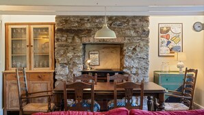 A dining area with a stone wall, wooden furniture, and a clock on the wall. - 19th Century Cottage & Garden, Private Parking (Cornwall)