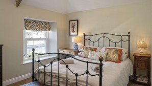 A bedroom with a bed, two bedside tables, a window with a curtain, and a wall-mounted lamp. - 19th Century Cottage & Garden, Private Parking (Cornwall)