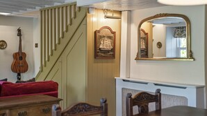 A room with a staircase, a framed poster, a mirror, a guitar, and a dining table. - 19th Century Cottage & Garden, Private Parking (Cornwall)