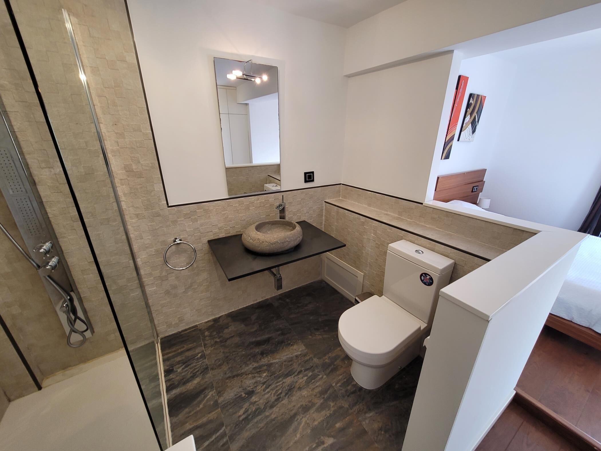 A modern bathroom with a glass shower enclosure, a round sink, and a toilet.
