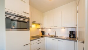 A modern kitchen with white cabinets, a stainless steel sink, a built-in oven, and a coffee maker. - Amazing Apartment on the First Floor (Middelkerke)