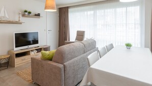 A modern living room with a sofa, a TV, a dining table, and pendant lights. - Amazing Apartment on the First Floor (Middelkerke)