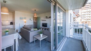 A modern apartment with a balcony, a dining area, a living room with a sofa and TV, and a kitchen with cabinets and a dining table. - Amazing Apartment on the First Floor (Middelkerke)