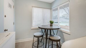 A corner room with a round table and two stools, a window with blinds, and a door with a handle. - Colorado Bay A & B (Colorado Springs)