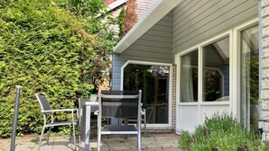 A patio with a table and chairs, a potted plant, and a building with a window.