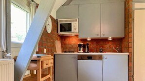 A kitchen with a microwave, stove, and sink, wooden shelves, and a patterned rug.