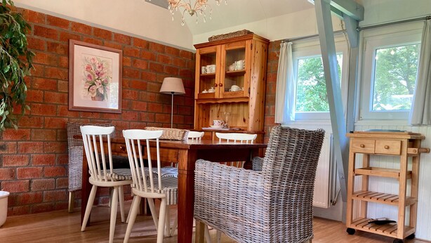 A dining area with a brick wall, wooden furniture, and a window with curtains.