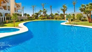 Une piscine au design incurvé, entourée de palmiers et bordée d’un bâtiment doté de balcons.