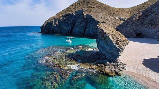 Un paysage côtier caractérisé par une eau turquoise cristalline, des formations rocheuses et une plage de sable.
