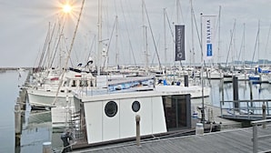 Un puerto deportivo con varios veleros amarrados, cielo despejado y el sol poniéndose o saliendo.