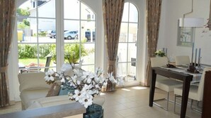 Una habitación con sofá, una mesa de comedor con sillas y amplias ventanas con cortinas.