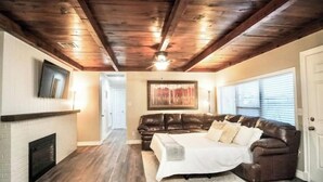 Ein Wohnzimmer mit Kamin, einem braunen Ledersofa, einem weißen Bett und einer Holzbalkendecke.