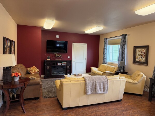 A living room with a fireplace, a television mounted on the wall, and a window with curtains.