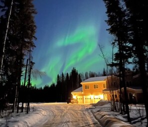 Una casa con un camino cubierto de nieve y una zona boscosa.