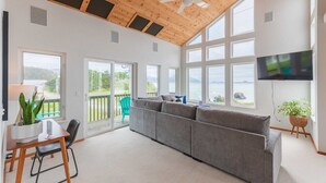 Ein geräumiges Wohnzimmer mit einem großen grauen Sofa, einer Holzzieldecke und einem an der Wand befestigten Fernseher.