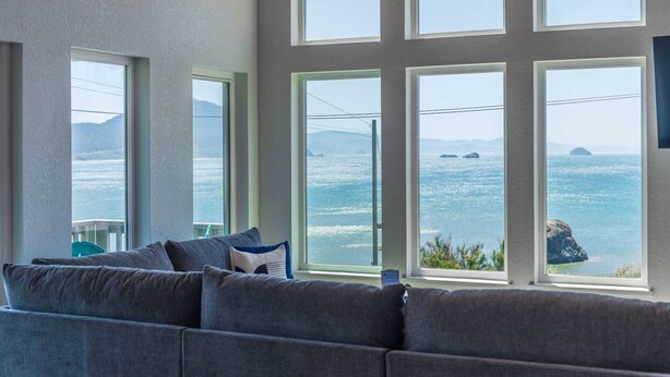 Ein Zimmer mit großem Fenster und Meerblick, ein graues Sofa und eine Ansicht ferner Inseln.