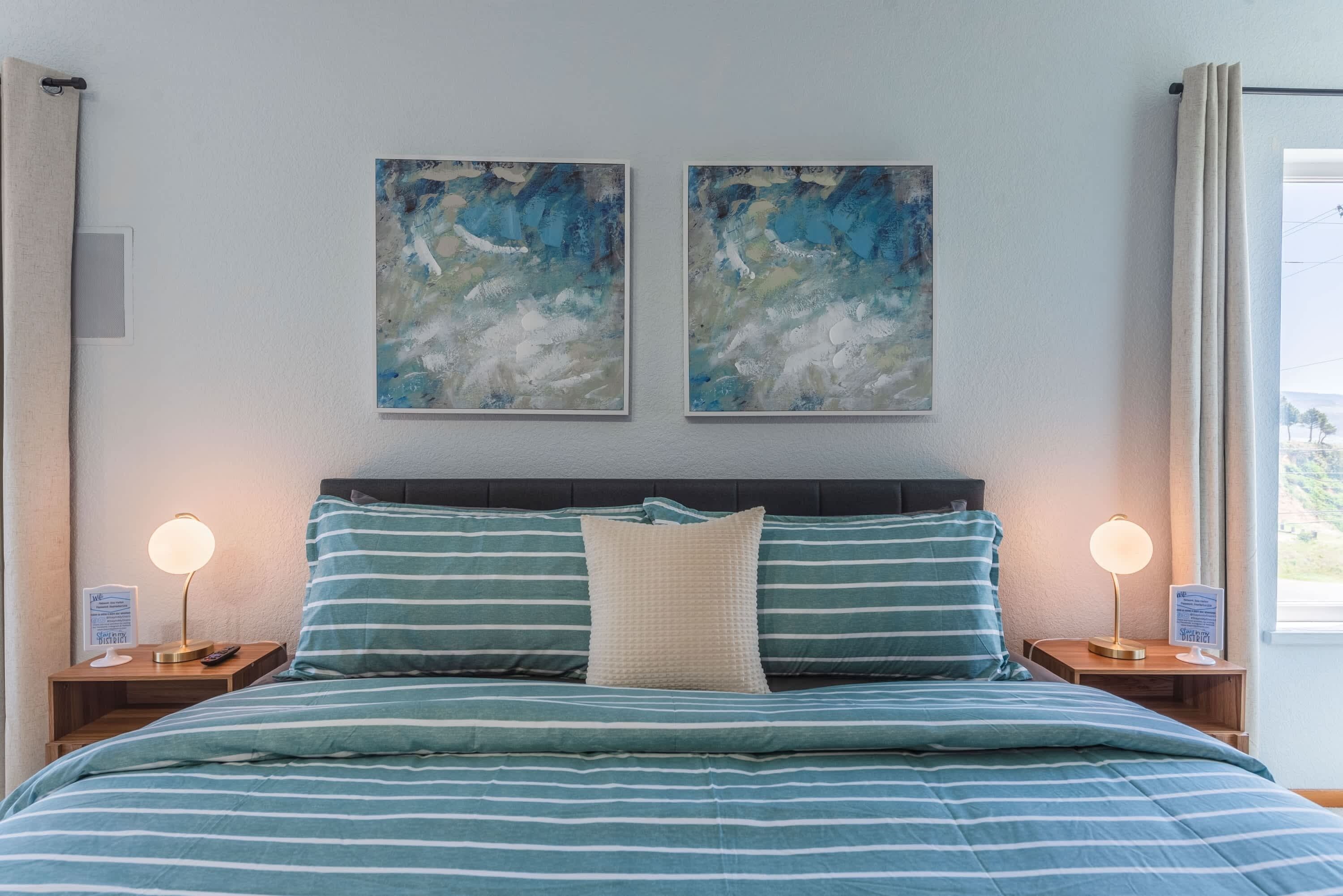 Un lit avec une literie à rayures, deux tableaux accrochés au mur et des lampes de chevet.