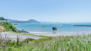 Eine Küstenstraße mit freiem Blick auf den Ozean, einem Sandstrand und fernen Bergen.