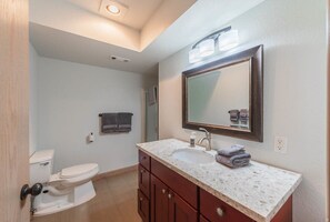 A bathroom with a white toilet, a sink with a marble countertop, and a mirror above the sink. - #StayinMyDistrict Ocean Overlook (Port Orford)