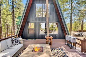 A modern A-frame cabin with a deck, a fire pit, and outdoor seating.